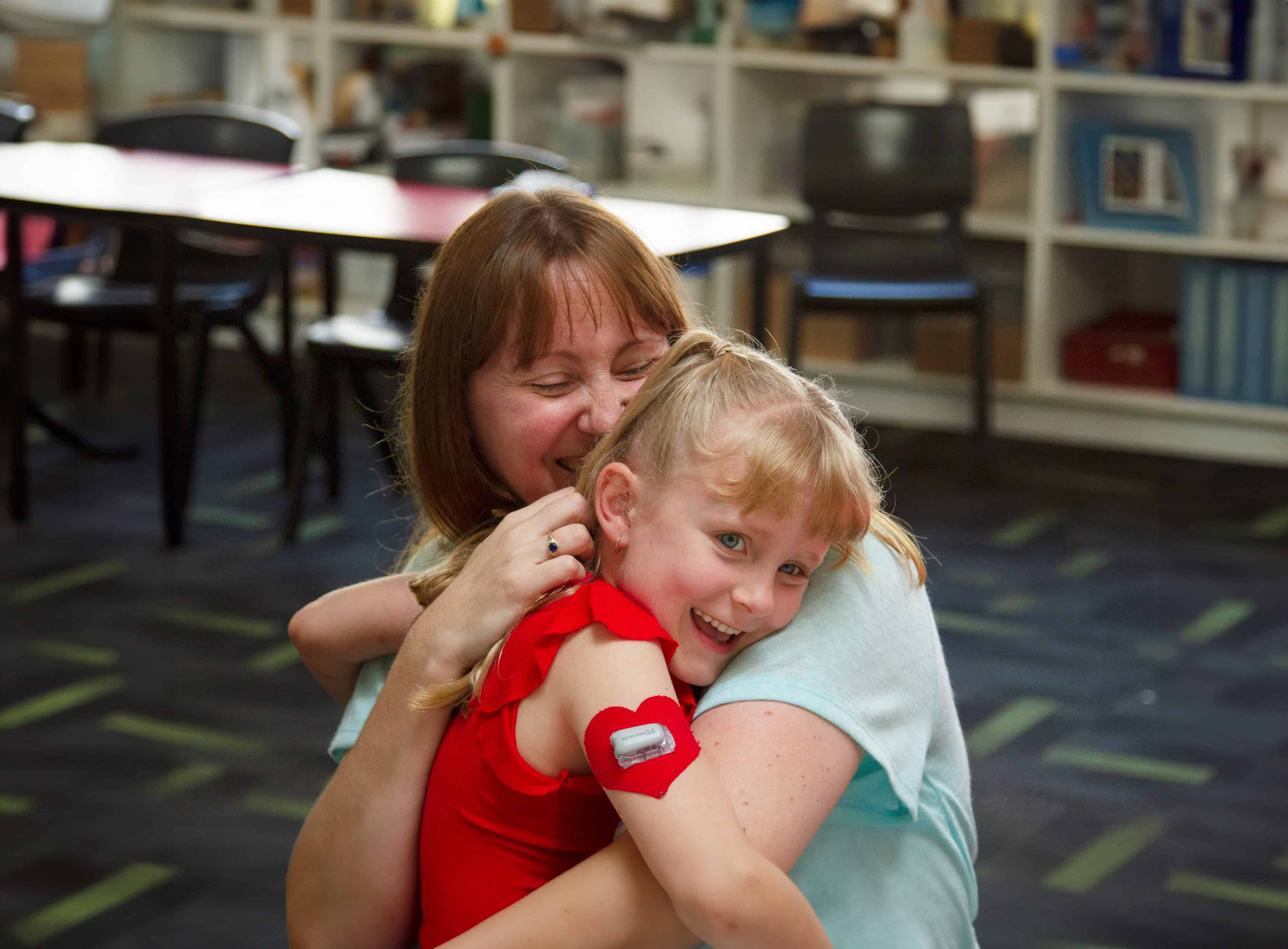 Mother cuddling young child with CGM on arm