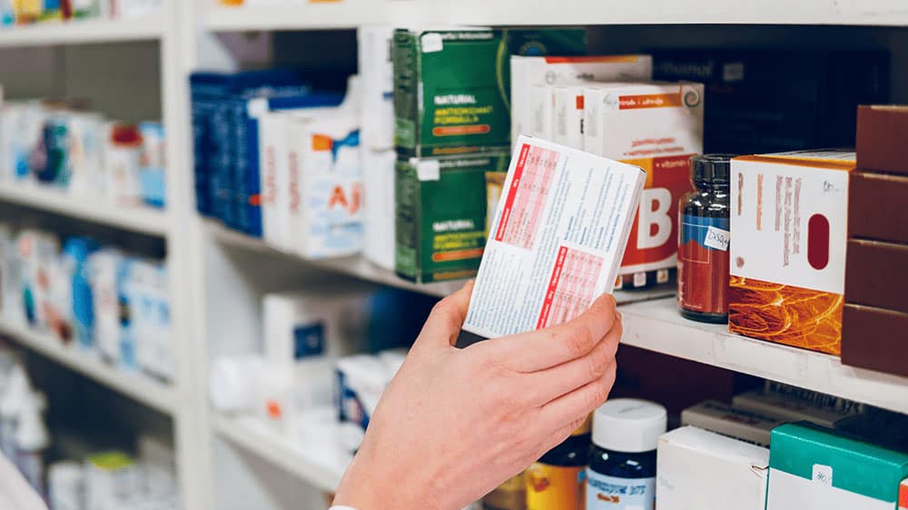 Hand selecting medicine from shelf of medications